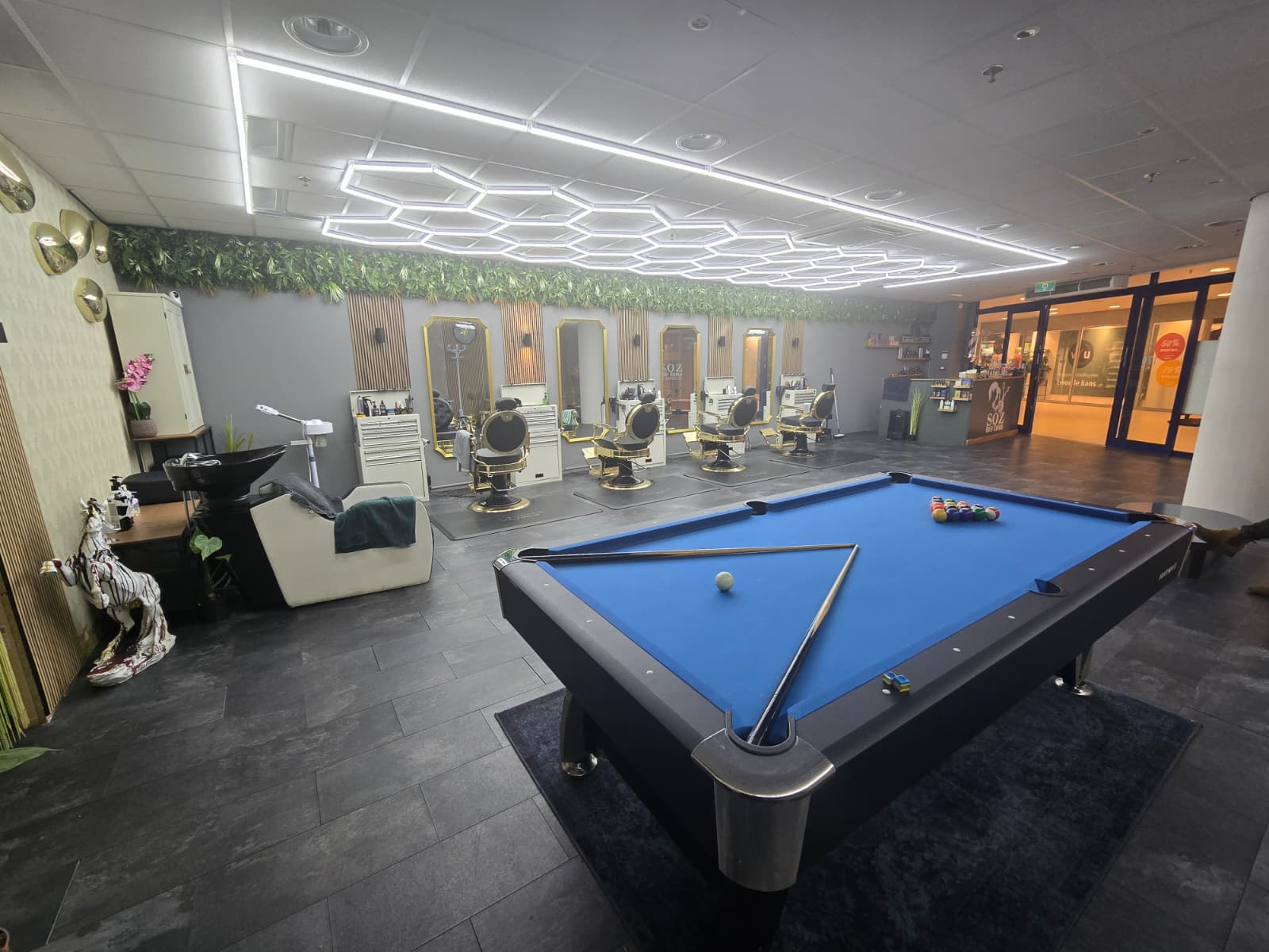 Een pooltafel met blauw laken in de zaak, met de kappersstoelen erachter