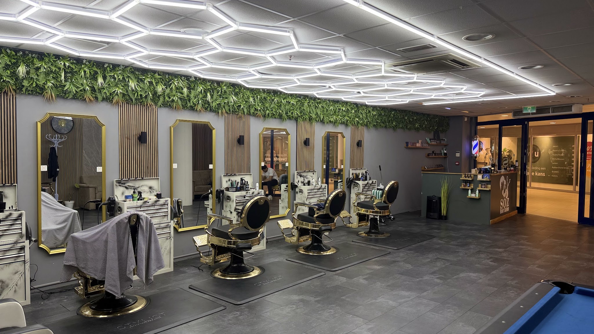 De zaak met een rij kappersstoelen, gouden spiegels, een groene wand en het zeshoekige lichtplafond